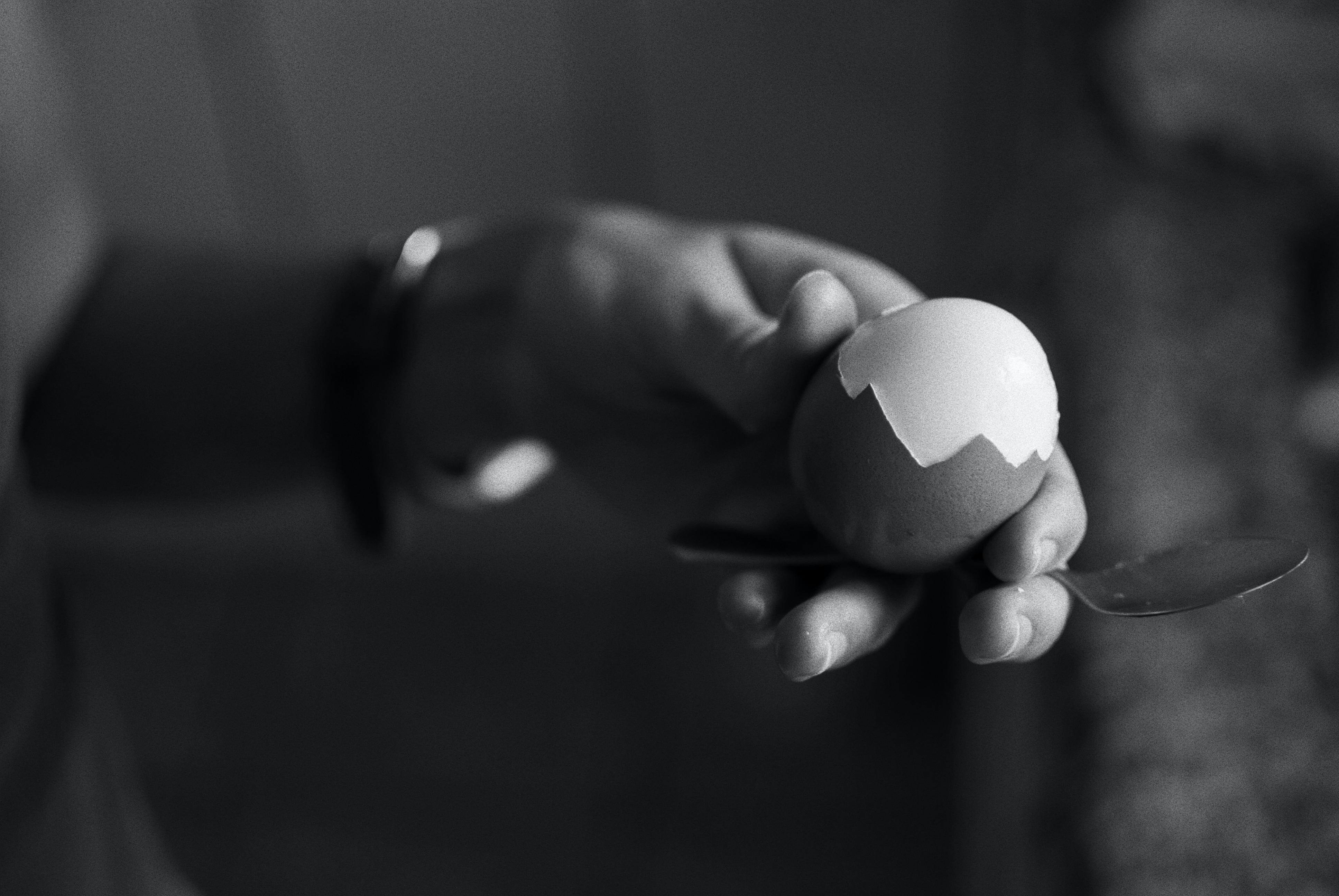 Black and white image of the hand of a woman showing a half-peeled hard egg.