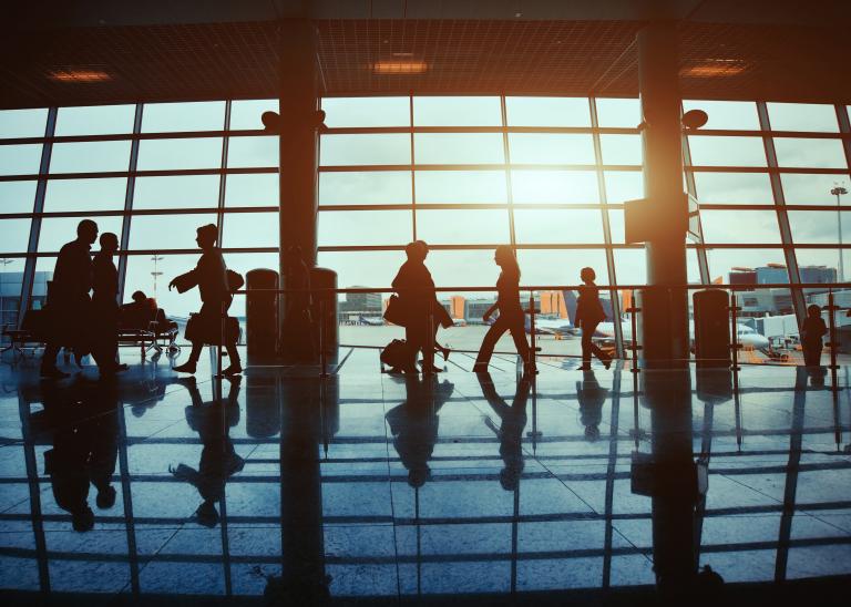 Silhouettes of unrecognizable people walking through an airport terminal for business travel.