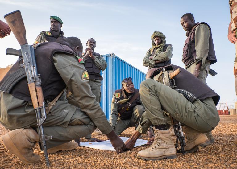Mali soldiers kneel and stand around a map conducting strategic planning for the Barkhane military operation in Mali.