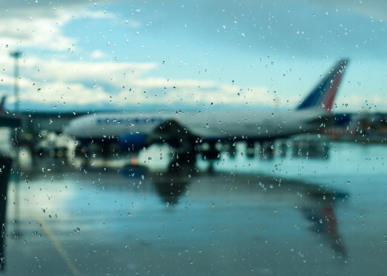 Un avion au sol vu à travers une vitre couverte de gouttes de pluie. 