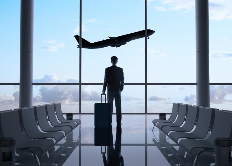 Business man stares at a plane taking off in the sky at the airport. 