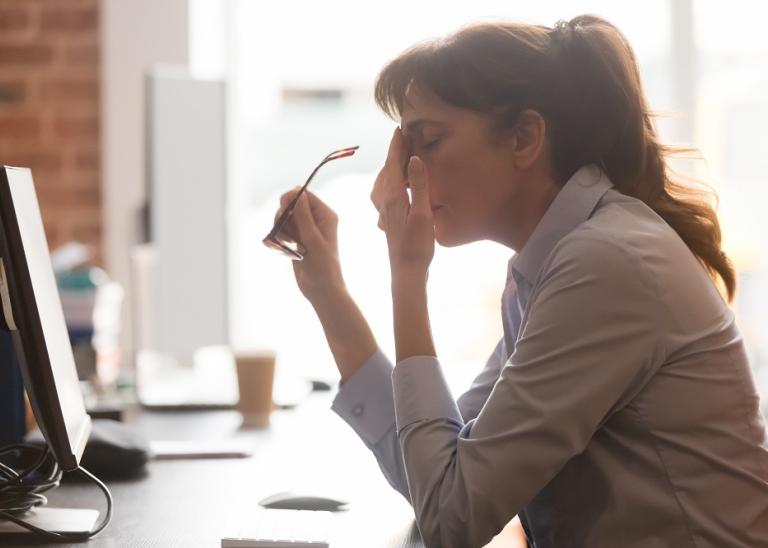 Exhausted female worker sit at office desk take off glasses feel unwell 