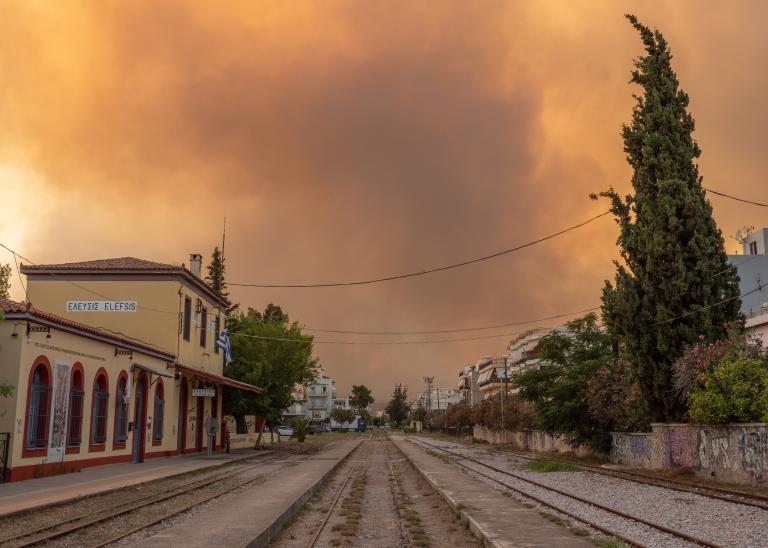 Smoke clouds from Europe and Mediterranean wildfires blaze over train tracks and buildings.