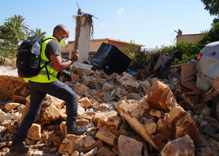 A person in a vest and mask, walking in rubble after floods from Storm Daniel in Libya.