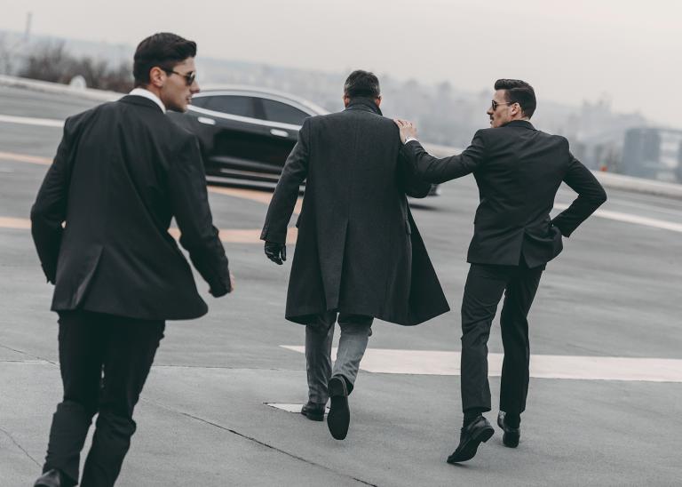 rear view of two bodyguards going with businessman to car