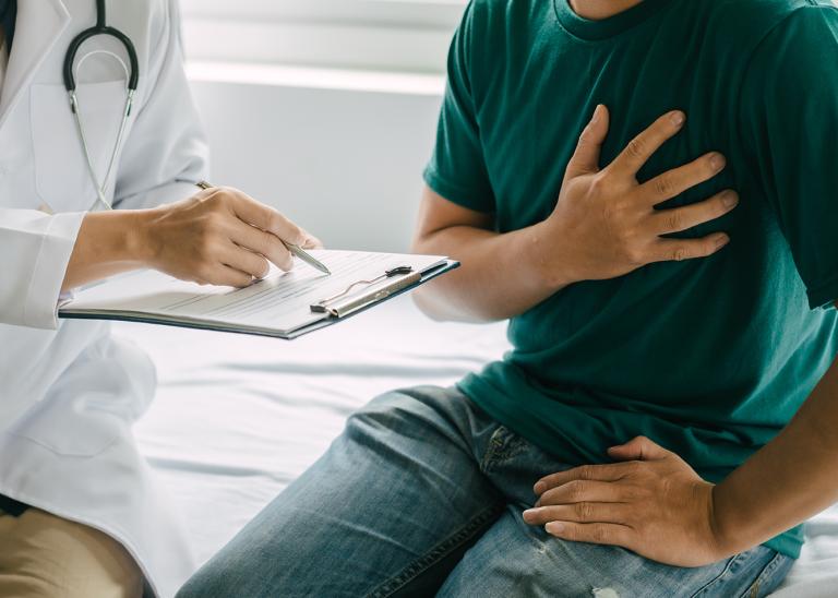 Doctor holding a clipboard assessing a patient with a hand on chest indicating chest pain