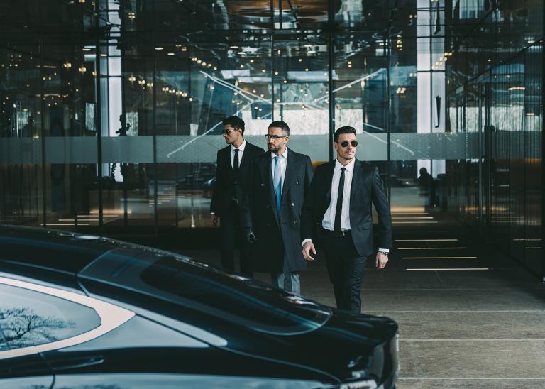 two bodyguards escorting an executive from building to a waiting car out front