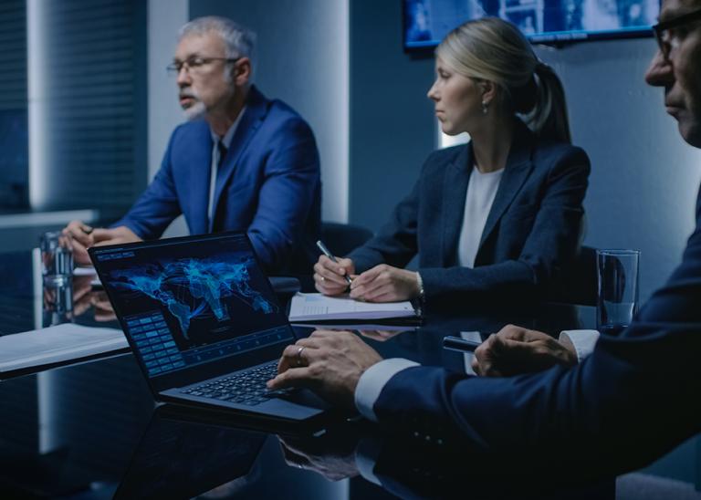 Employees sitting around a situation room looking at maps on their laptops