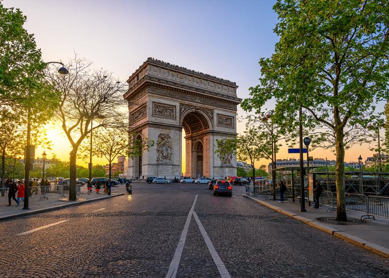 Champs elysee pictured from a street view with the sunrise or sunset behind it.