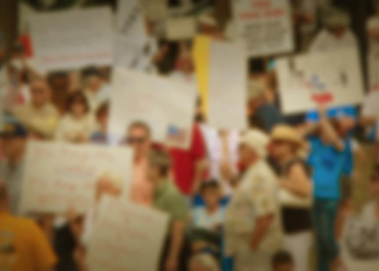 crowd of people holding signs and flags in united states at a political rally but faces and signs are blurred 