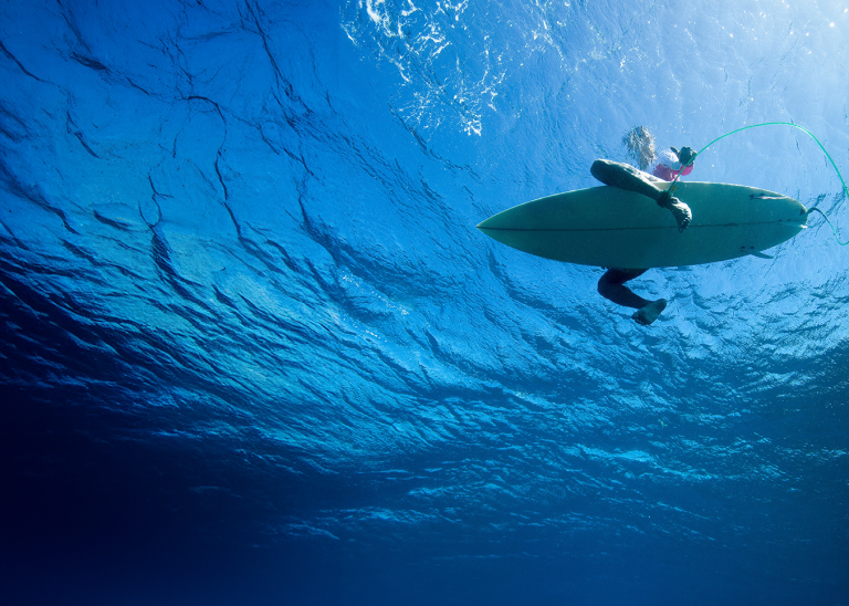 a look up at a surfer from below in clear blue ocean water