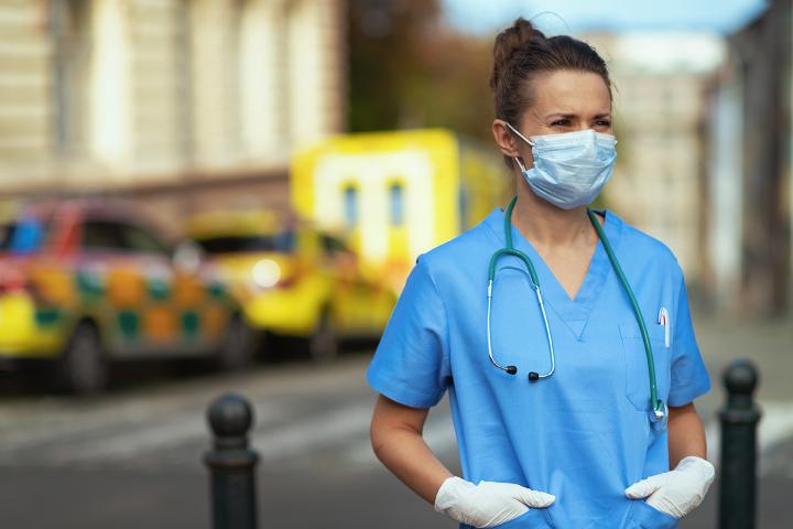 Nurse standing outside of hospital to represent healthcare infrastructure.