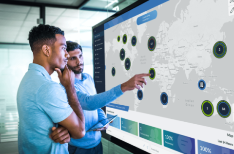 two workers discuss a location while looking at a world map on a screen using critical event management software