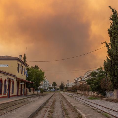 Smoke clouds from Europe and Mediterranean wildfires blaze over train tracks and buildings.